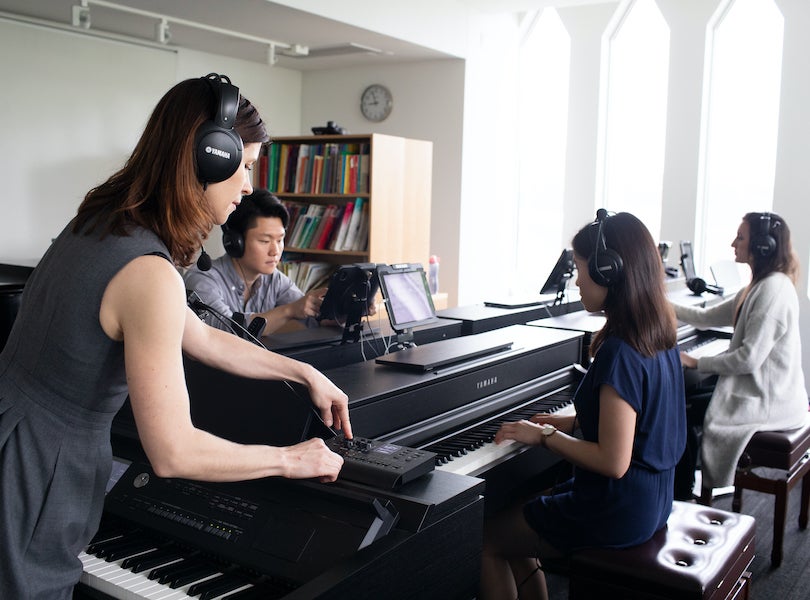teacher working with students at keyboards in a piano pedagogy lab.