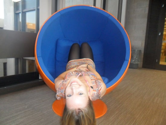A girl laying in a wombchair backwards, so that her feet are at the head and her head is spilling out of the mouth 