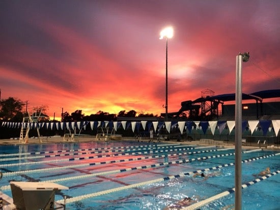An outdoor pool lined with swimming lanes. The sky above is a beautiful pink, purple, and yellow