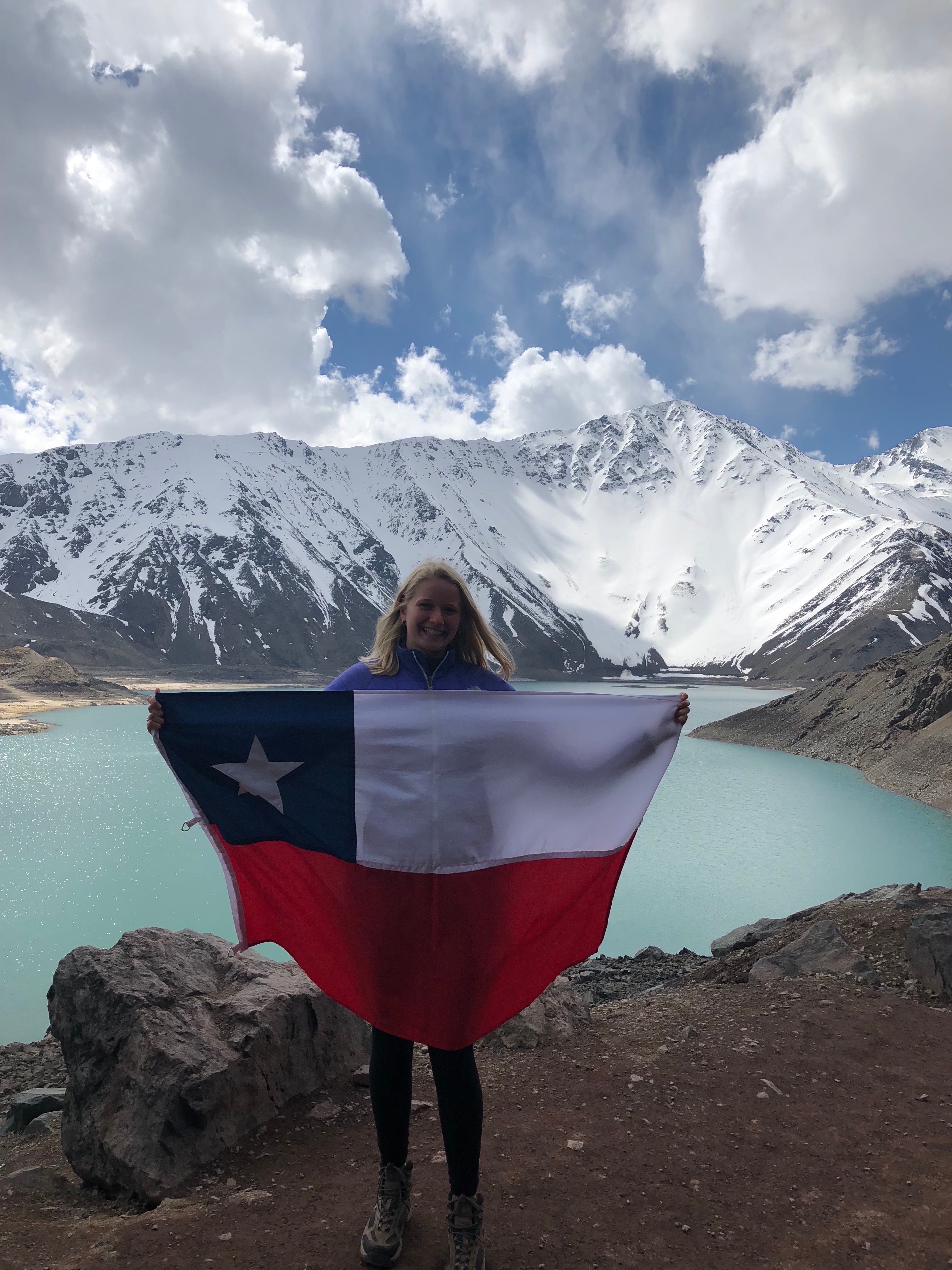 Sarah holds a Chilean flag with mountains and a lake in the background