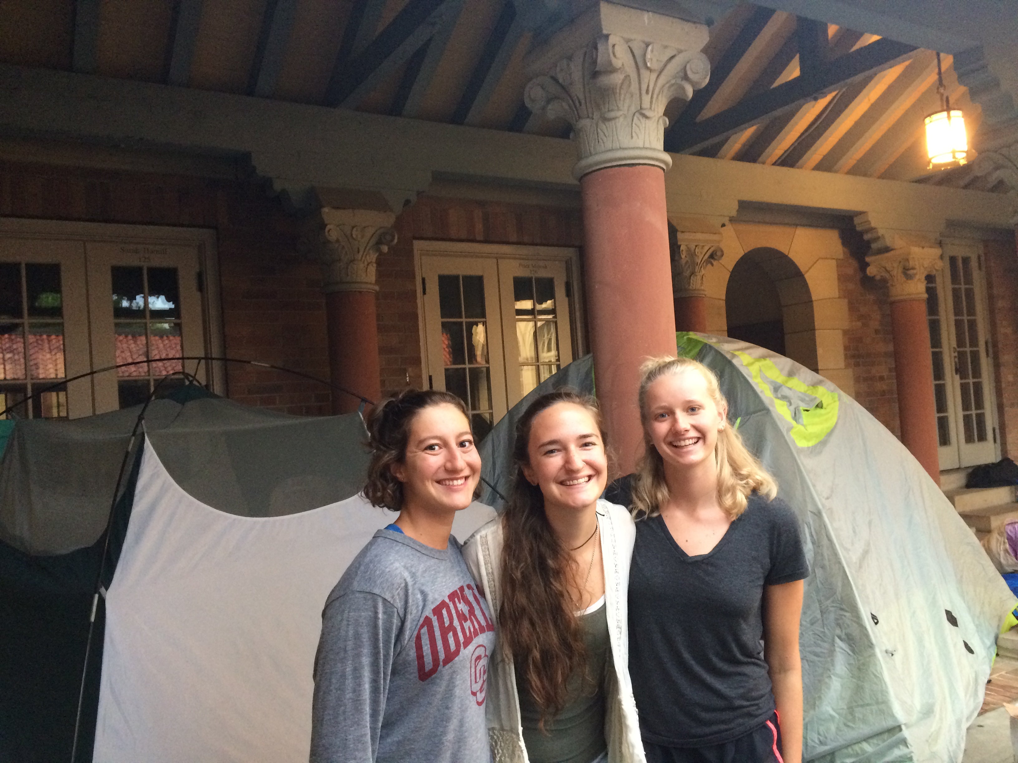 three college students stand smiling in front of a tent
