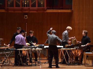 director leads5 percussion players in rehearsal. photo.