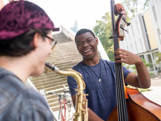 A sax player and a bass player jam outdoors.