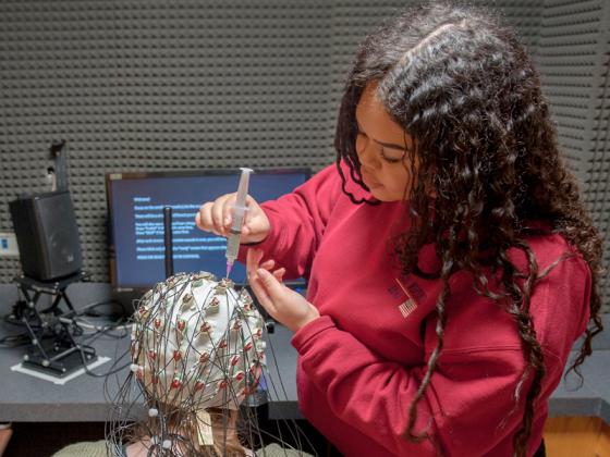 A student attaches wires to another student's head.