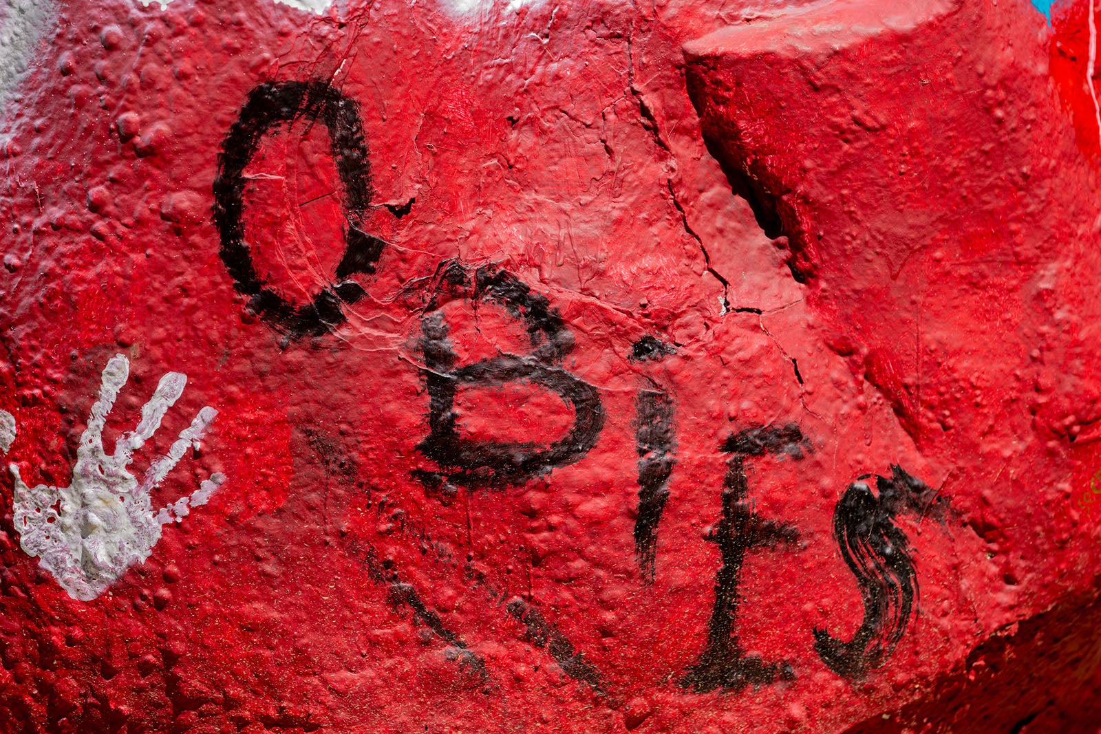 A close-up of a red painted rock with the word 'Obies' painted across it, plus a white handprint.