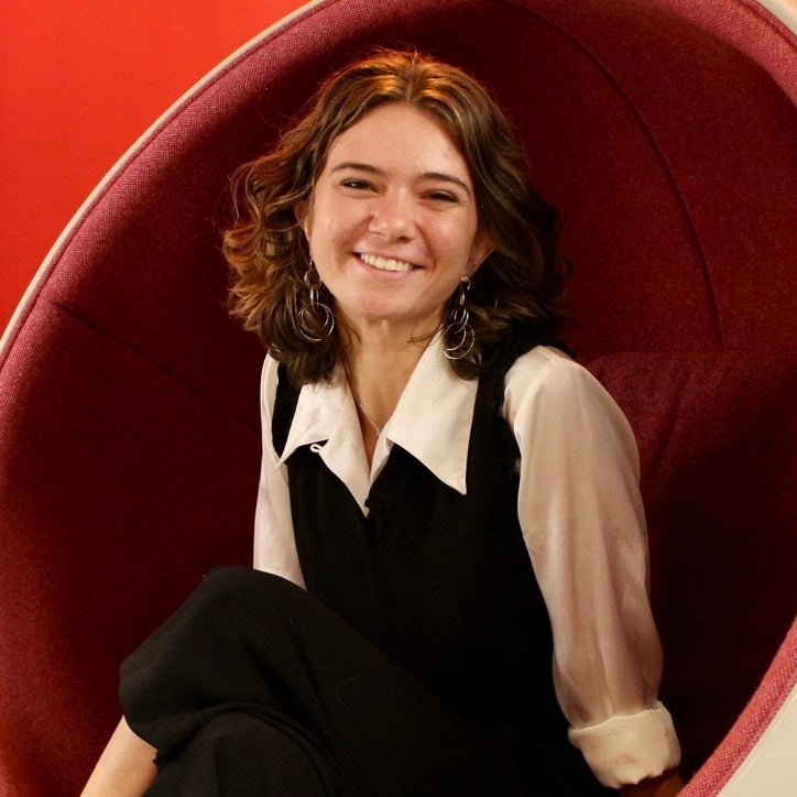 A female-identifying student wearing white shirt, sitting in a red chair.