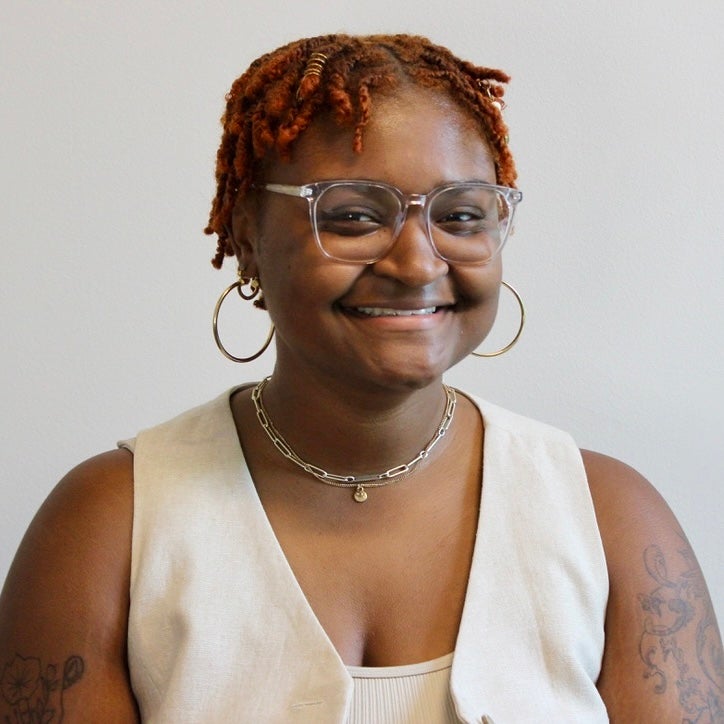 A headshot of a non-binary student  with short red hair and glasses.