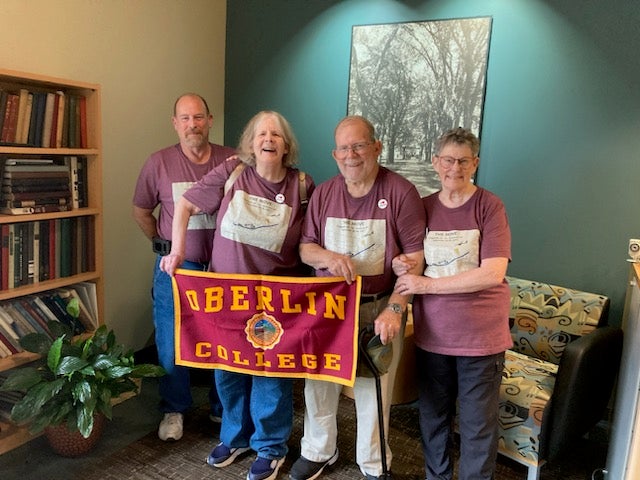 The four members of the Harbison family at Oberlin. They are wearing matching t-shirts and holding an Oberlin College banner.