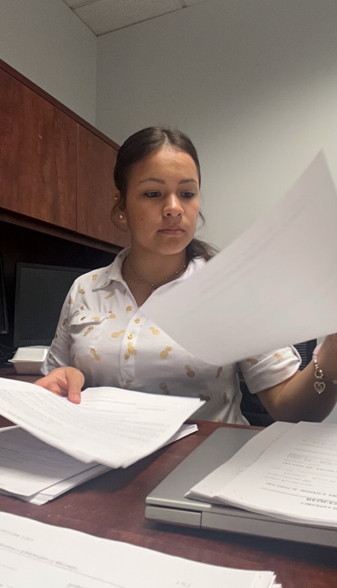 Woman holds papers at desk.