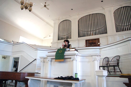 A professor speaking from behind the pulpit. She stands in front of a giant white organ