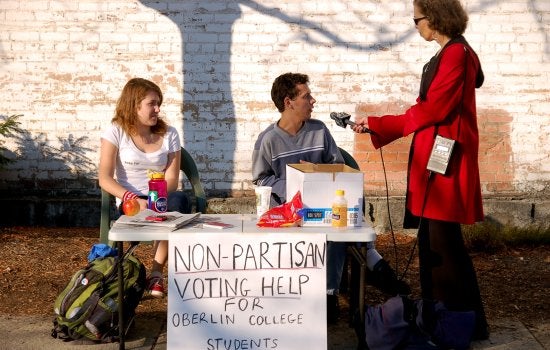 Students sit at a table and are being interviewed by a woman with a microphone
