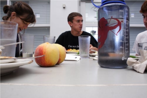 A table level view of a students sitting at a table in Stevie. In focus are two peaches and a Nalgene water bottle