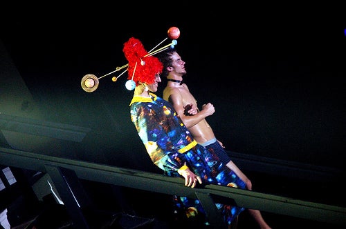 A performer wearing a red wig and a space themed dress. She is accompanied by a boy wearing only his underwear 