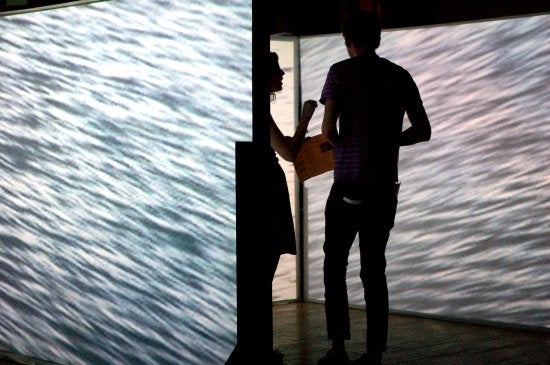 Two people stand in a room of screens featuring water 