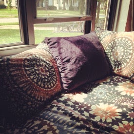 a neatly made bed by a window, with many pillows