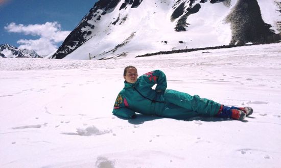 A girl wearing a turquoise snowsuit lounging in the snow