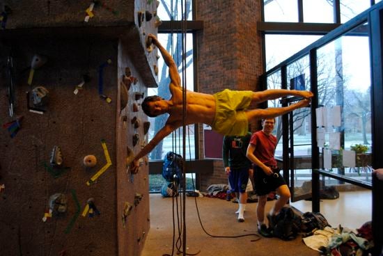 The rock climbing wall in Phillips gym. A climber is free climbing without a harness and is positioned horizontal to the ground
