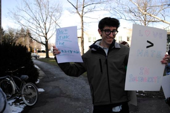 A student holds protest signs: "Love > hate; in solidarity"