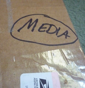 A box is taped up for shipping, with the word Media handwritten with a marker