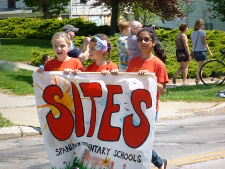 3 kids carry a banner: SITES Spanish in the Elementary Schools