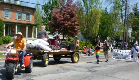 A wagon pulls a drummer playing a full drum kit, along with amplifiers, followed by marching electric guitarists.