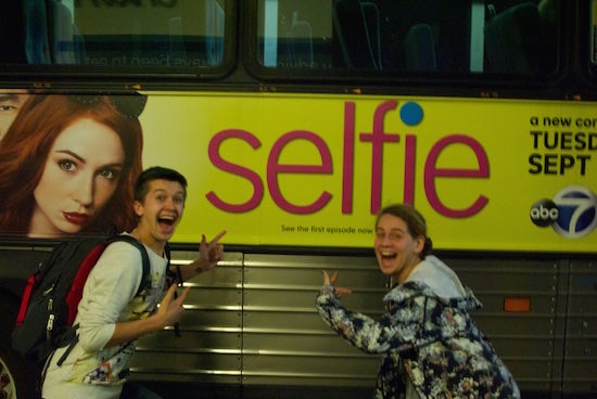 Two people point to an advertisement with the word "selfie"