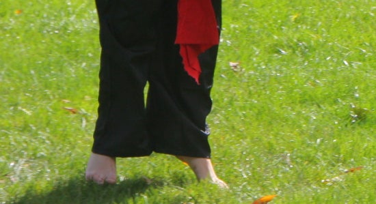 Closeup of bare feet in the grass, heels off the ground.