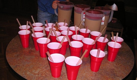 Many red cups with wide straws, and 4 pitchers of tea.