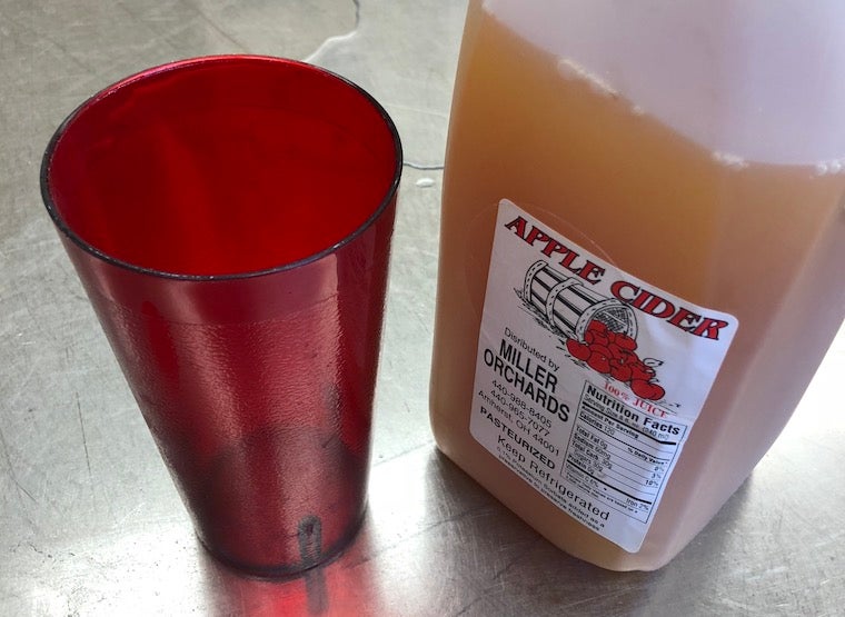 A red cup next to a jug of apple cider
