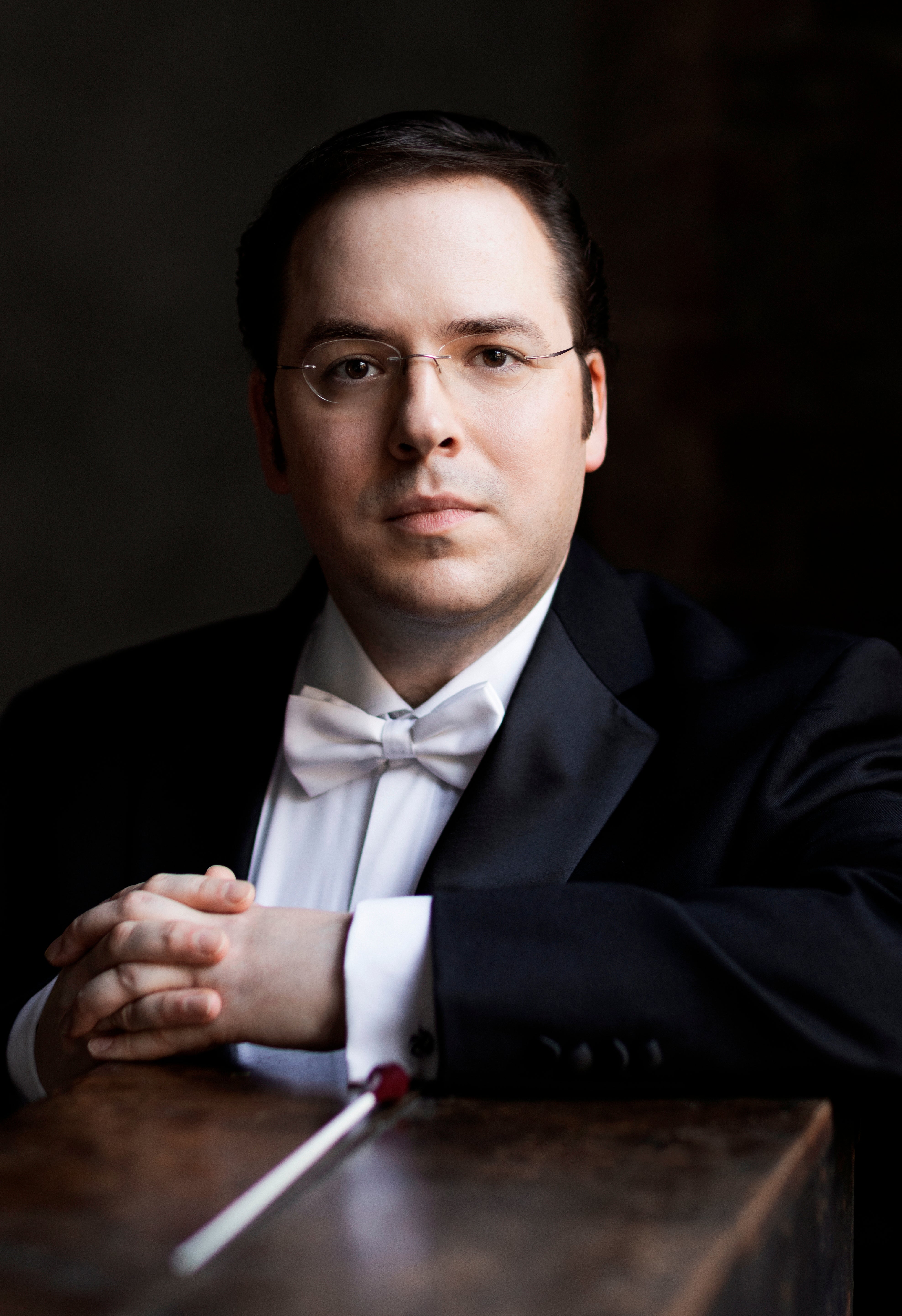 man wearing tuxedo with baton resting in front of him