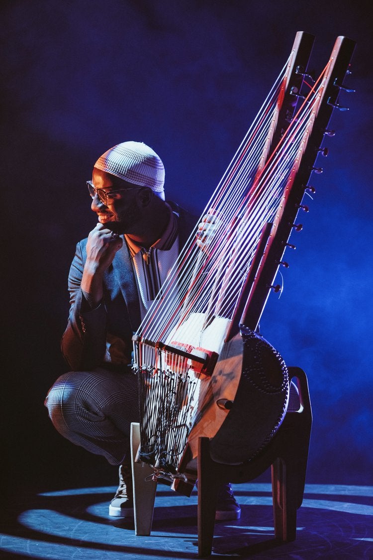 man on a stage, playing a stringed instrument called a kora