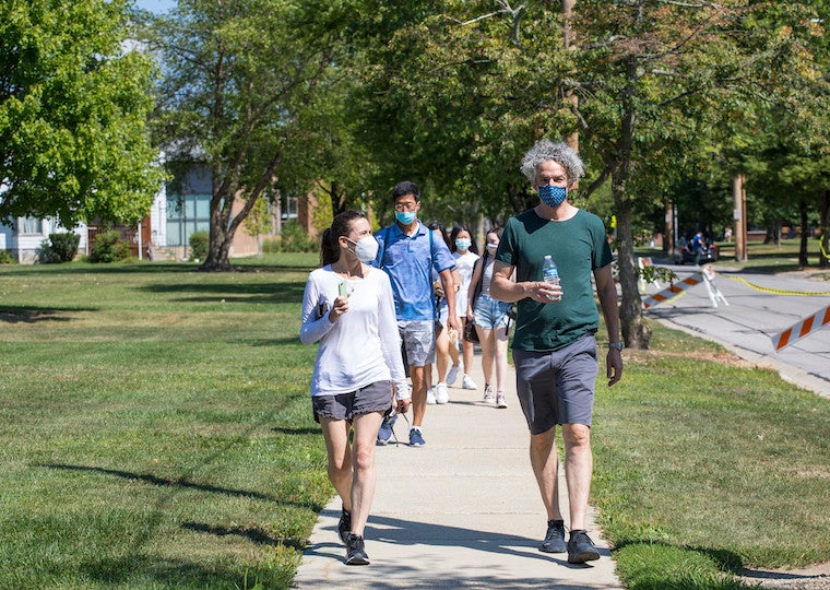A crowd of parents wearing masks walk down a street.