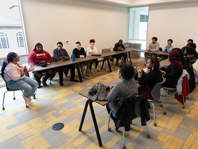 A group of students sit facing a graduate student in a conference room.