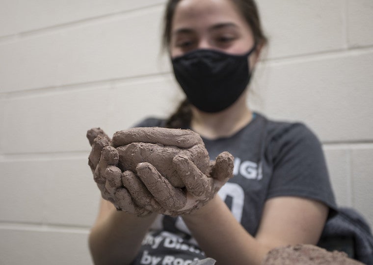 A girl holds a wet clay pot