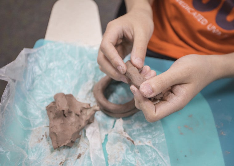 Hands of a student hold a long piece of clay.