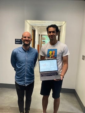 Student poses with professor while holding computer.