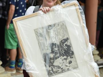 Student holds a framed drawing, which is wrapped in plastic.