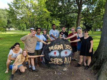happy students gathered around a painted rock that reads "Mama 'Sco Sees All."