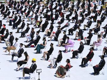 Alarge number od graduates sit 5 feet apart in a football field.