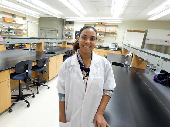 A young black woman in white lab coat standing in a lab.