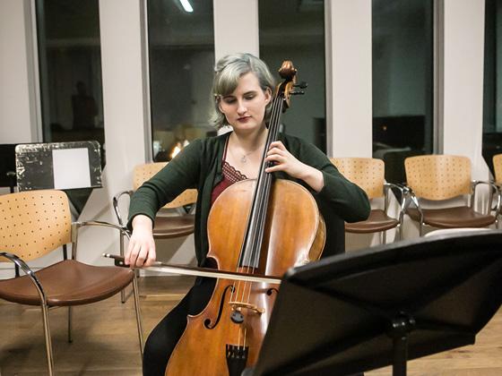 A young woman practices her cello in a large practice room.