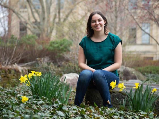 Amelia, in green shirt and jeans, sits on a rock surrounded by daffodils.