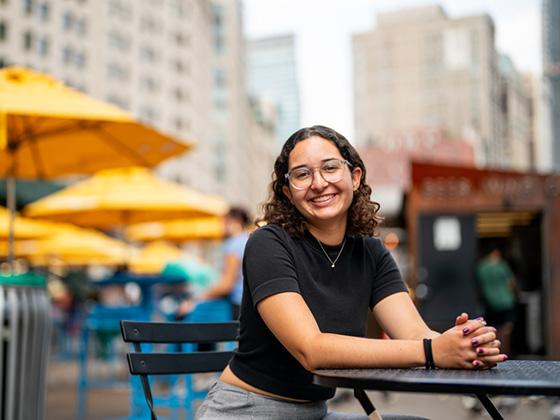 Noah is seated at an outdoor cafe table in the city.