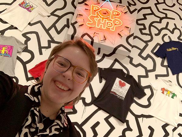 Cecil in front of a wall of Keith Haring tee shirts and a neon sign that says Pop Shop.
