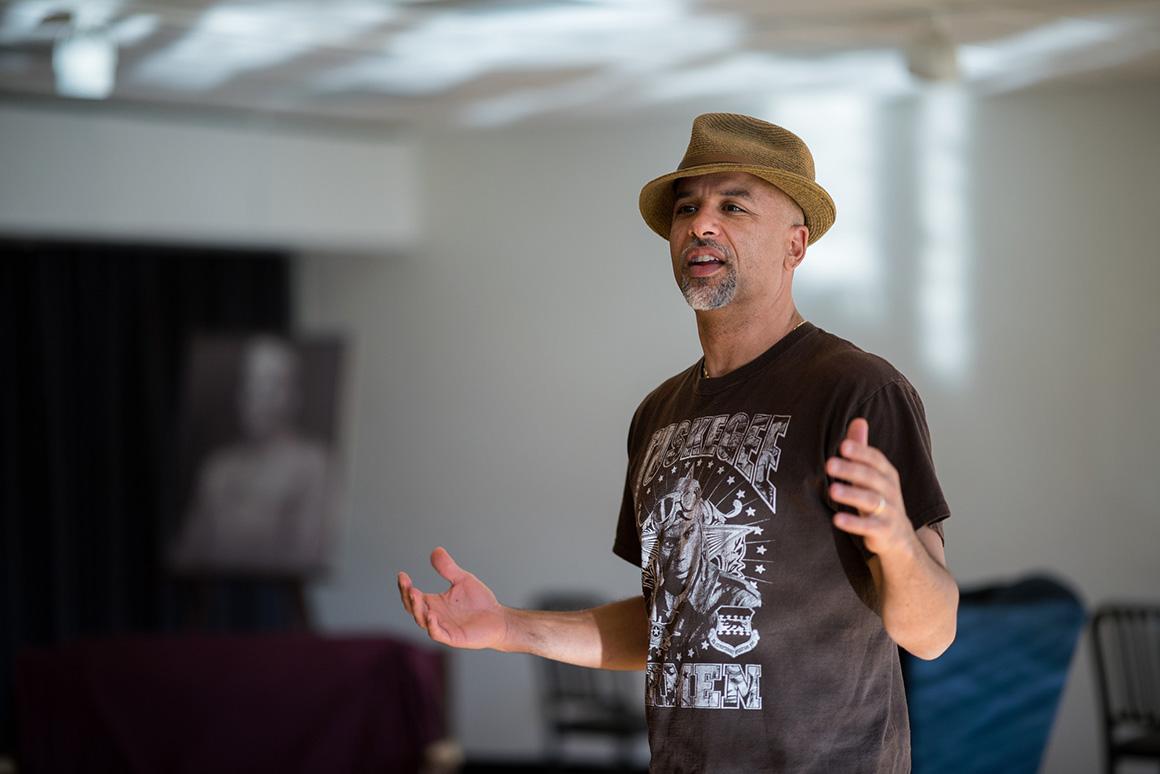 A professor in a fedora-style hat teaches in a drama studio.