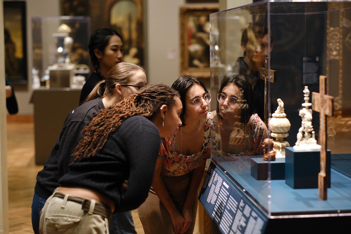 Students lean toward a glass museum case to view artifacts.