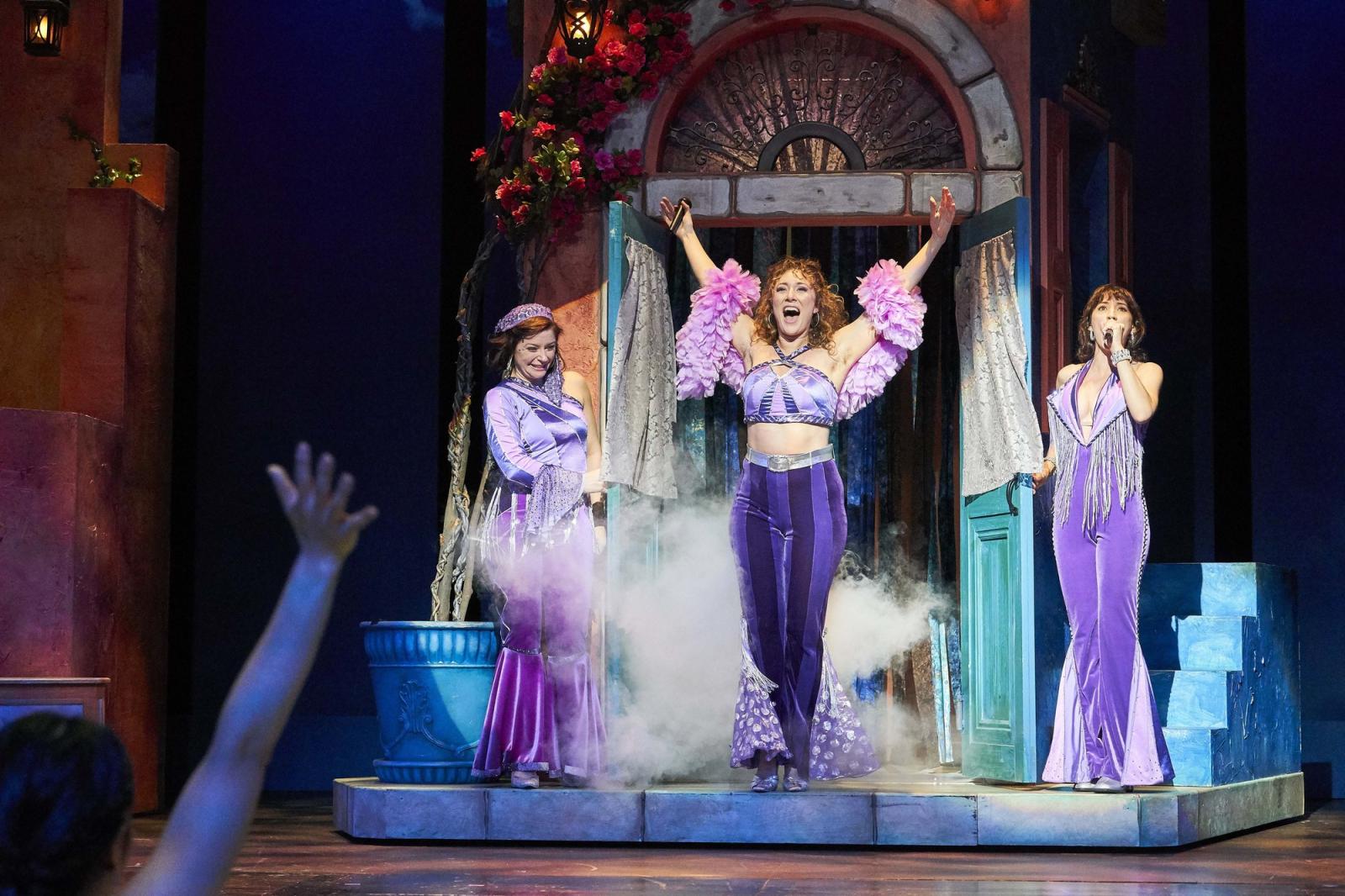 Three women in costume sing and dance.