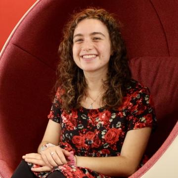 A female-identifying student wearing a floral shirt, sitting in a red chair.