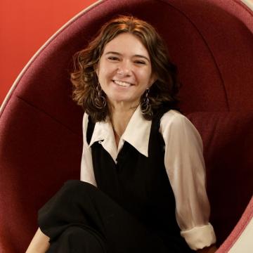 A female-identifying student wearing a white shirt, sitting in a red chair.