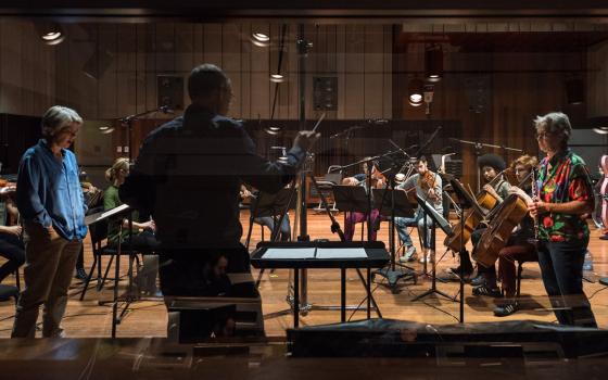 Musicians recording in a studio, as seen from the control room through the glass divider.